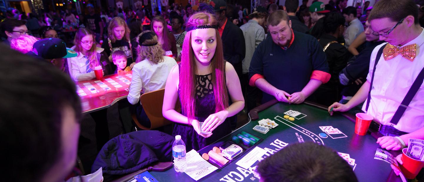 学生计划委员会网页横幅图像, 一个拥挤的房间描绘了一个赌场之夜, 一个打扮成少女的女孩在桌子上发牌